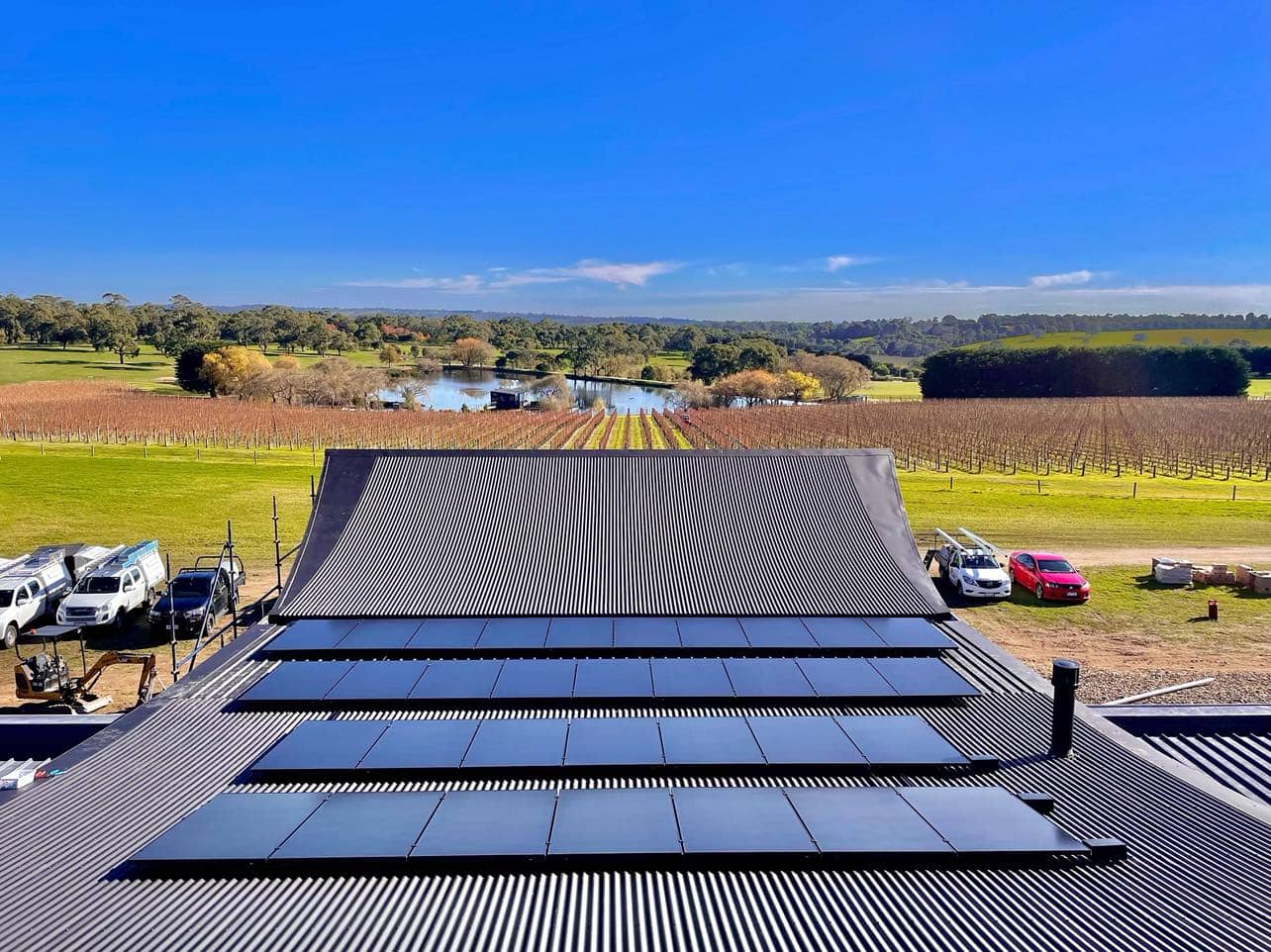 Solar panels on a curve roof overlooking a green paddock with a bright blue sky.