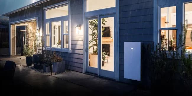 A Tesla Powerwall Home Solar Battery on a grey weatherboard house.